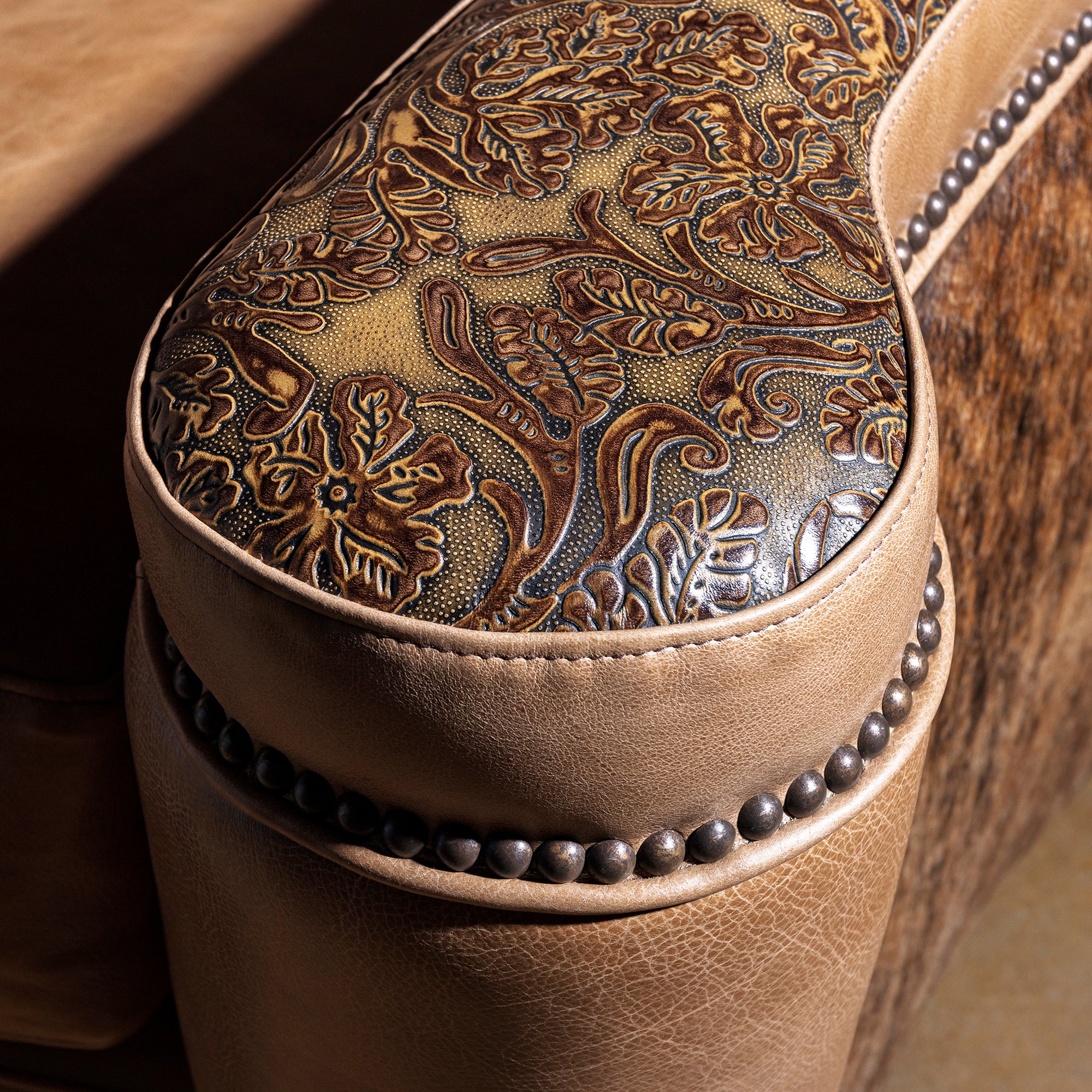 Close-up of tooled leather arm cap with nailhead trim on Western leather sofa