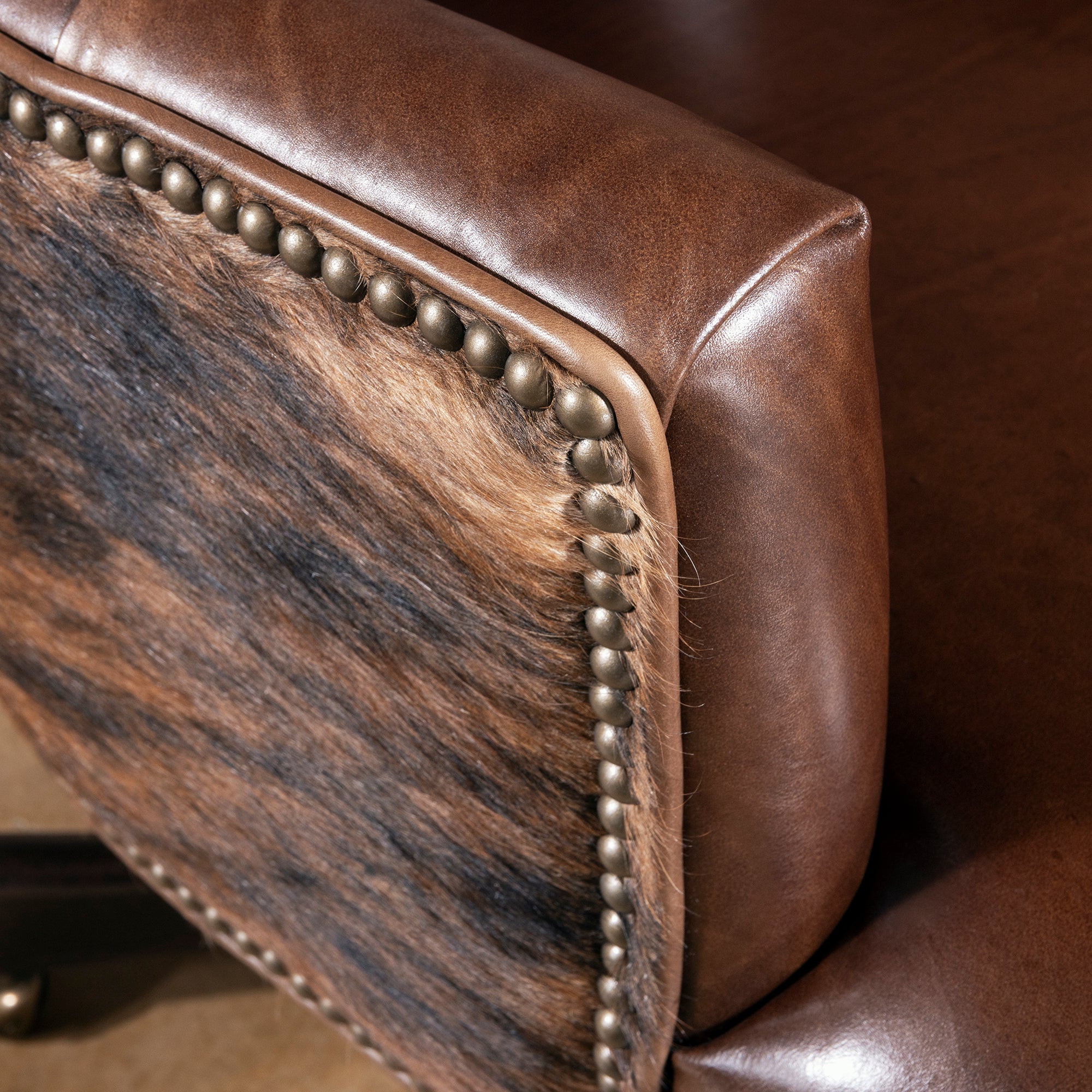 Close-up of armrest, nailhead trim, and brindle cowhide side panel on swivel desk chair
