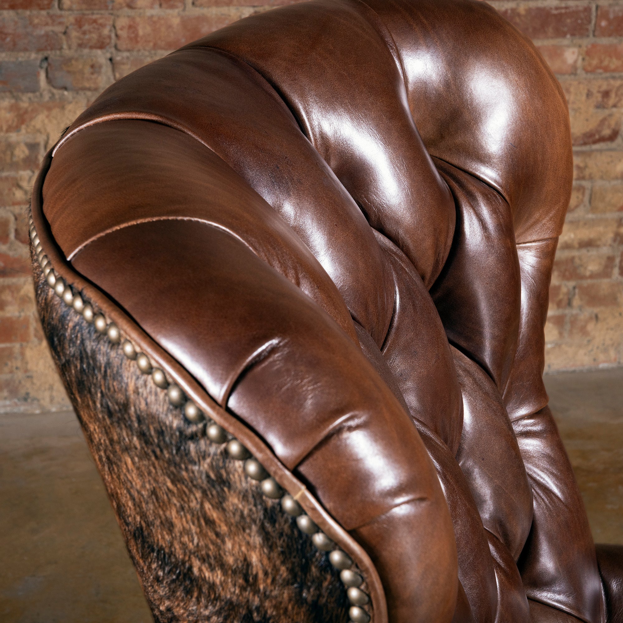 Close-up of tufted leather back and curved arm on brindle cowhide Western desk chair with nailheads