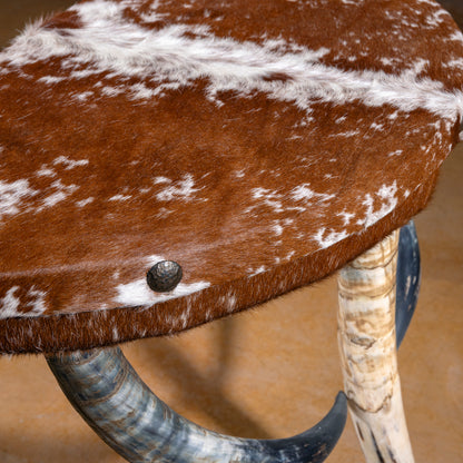 Close-up of speckled cowhide upholstered top with nailhead accents on demi-lune table