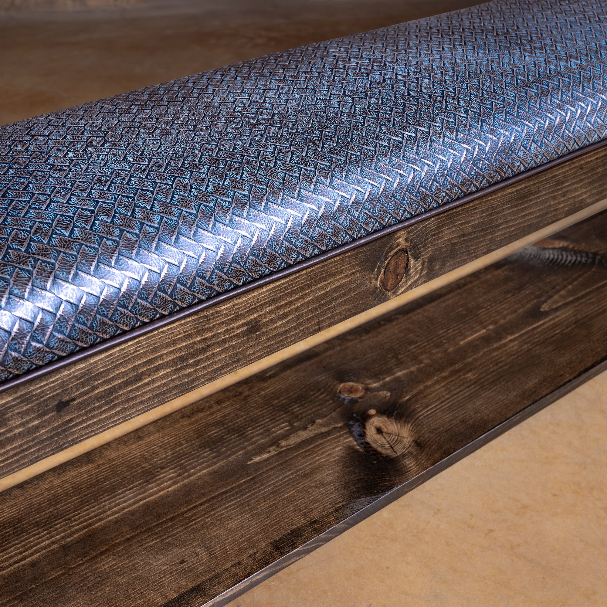 Angled view of silver-blue leather bench with basketweave texture, dark wood frame, and open shelf storage