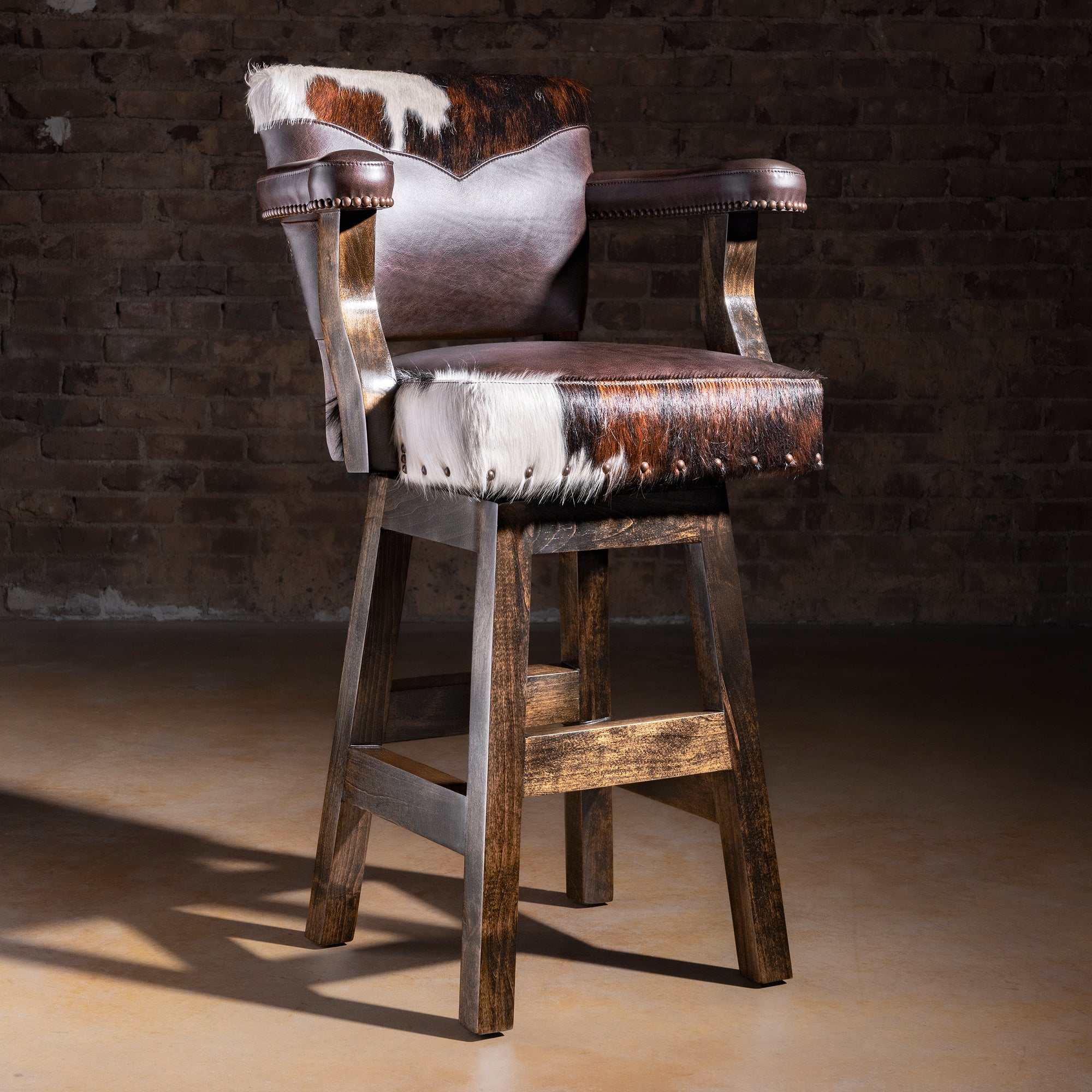 Cochise tricolor Brazilian cowhide and dark leather Western bar stool with arms, nailhead trim, and rustic Alder wood base