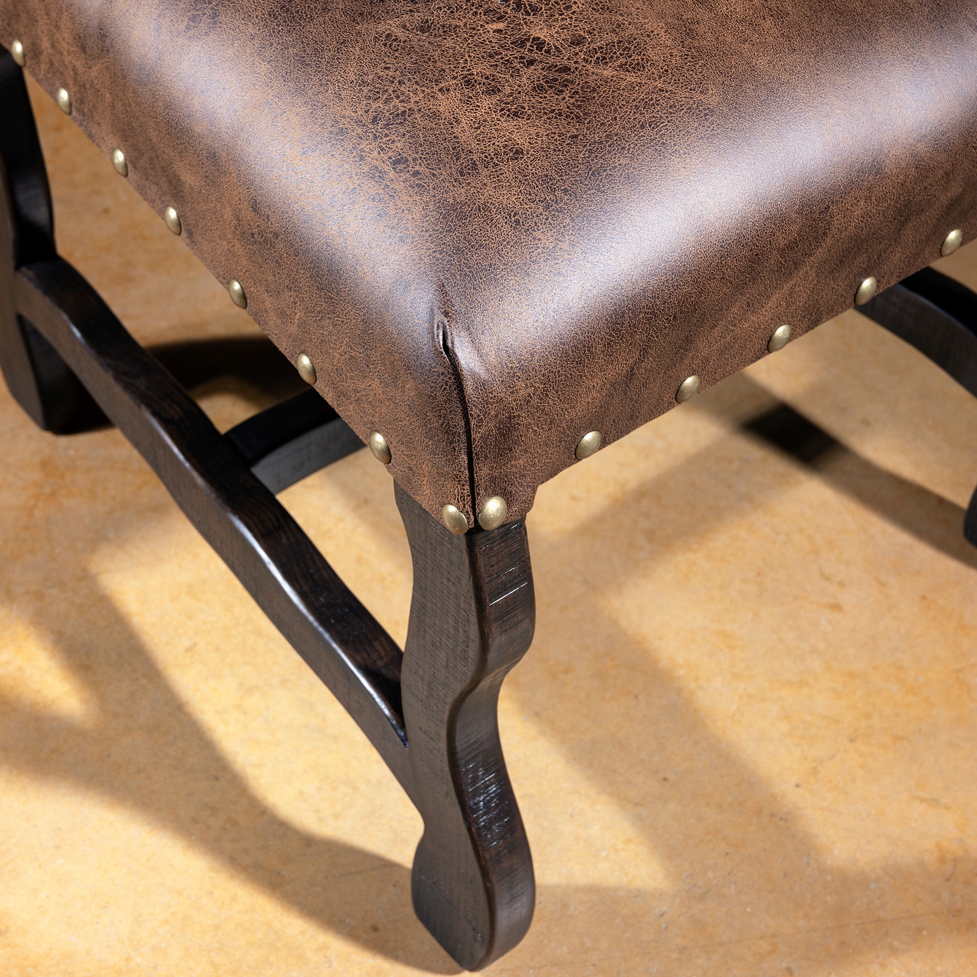 Closeup of distressed leather seat with nailhead trim and dark wood base on Western dining chair, rustic luxury dining seating