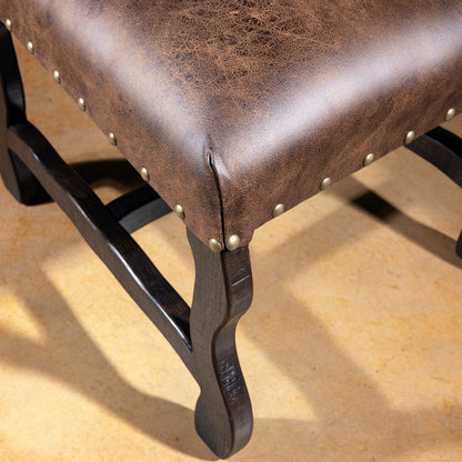 Closeup of distressed leather seat with nailhead trim and dark wood base on Western dining chair, rustic luxury dining seating