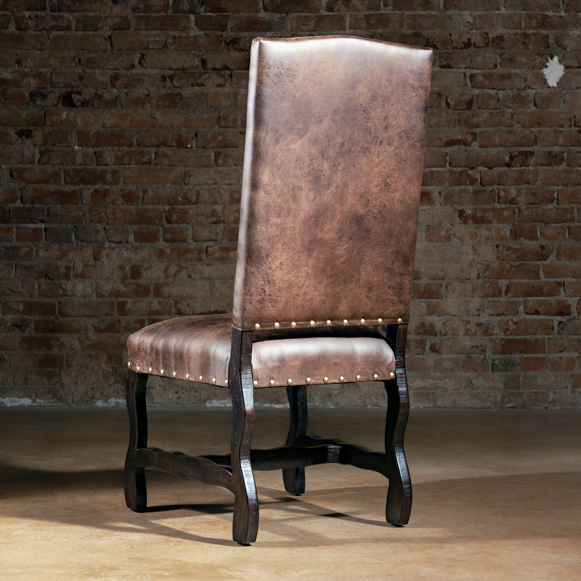 Back view of Western leather dining chair with tall silhouette, brass nailheads, and dark wood legs, rustic ranch dining room seating