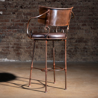 Back view of copper-toned Western bar stool with forged iron arms and scroll details