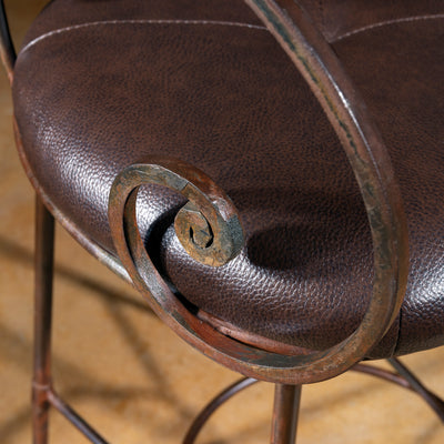 Close-up of forged iron scrollwork arm detail on copper back leather seat bar stool