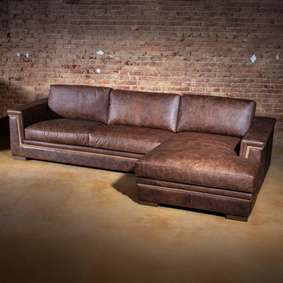 Rustic brown leather chaise sectional sofa styled against exposed brick wall for a modern Western look
