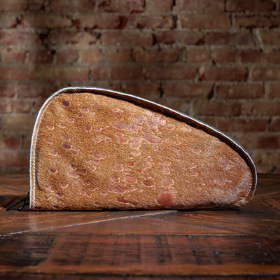 Tan cowhide gun case with natural gold fleck pattern on rustic wood table