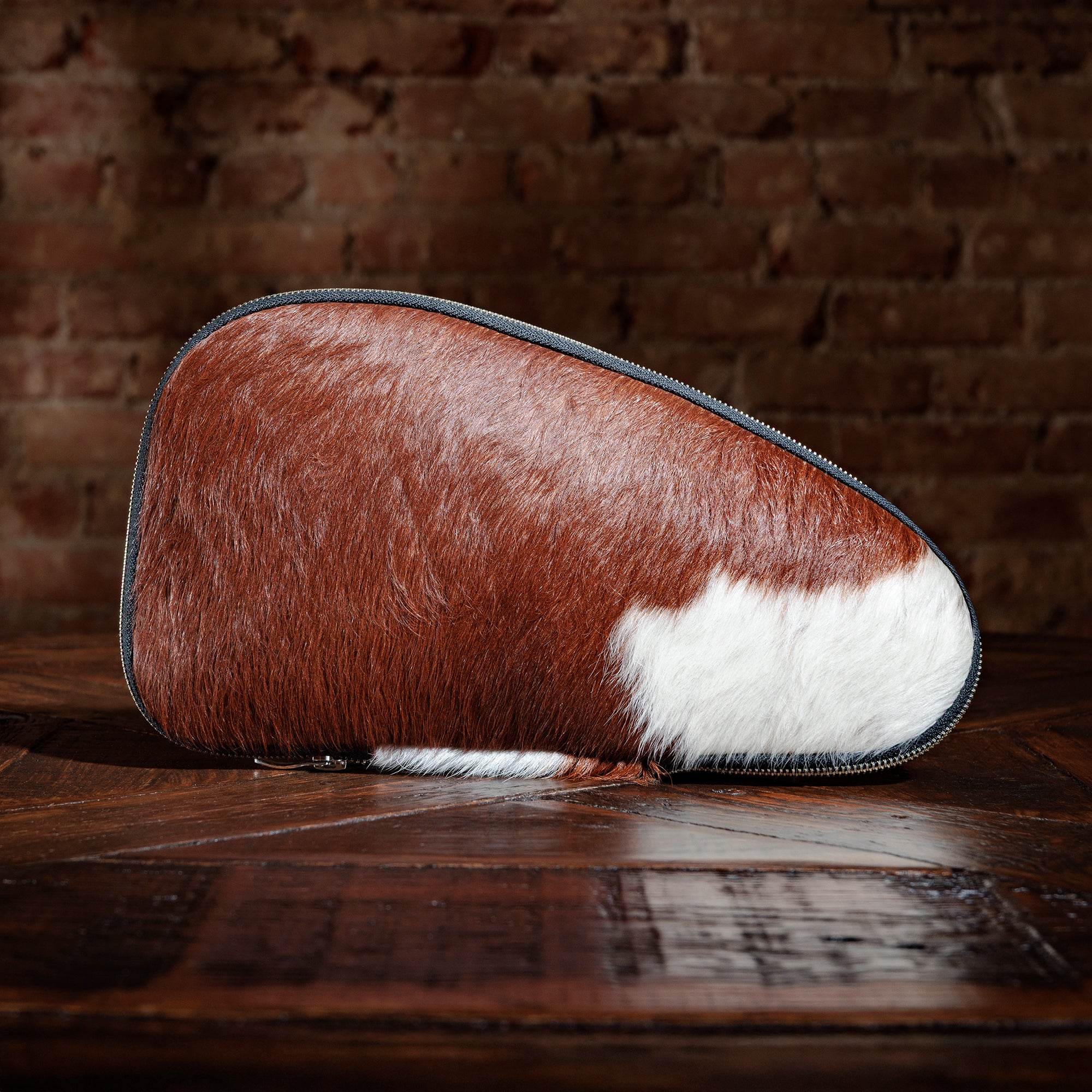 Chestnut and white cowhide gun case with zipper on rustic wood table