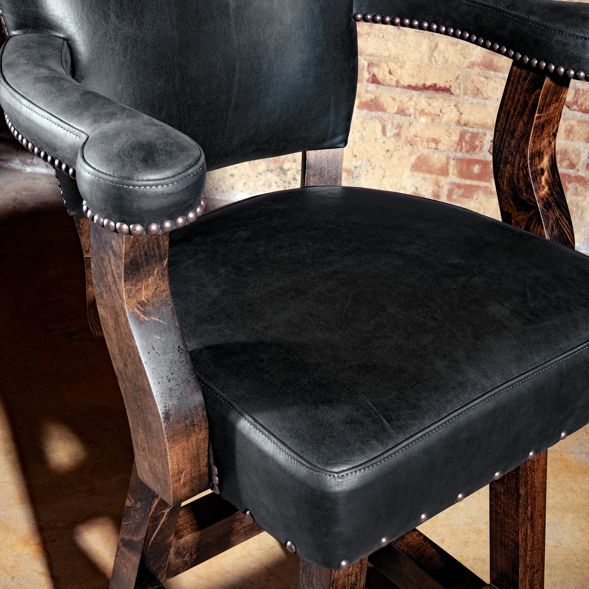 Close-up of black leather seat and armrest with hand-applied nailhead trim on wood frame.