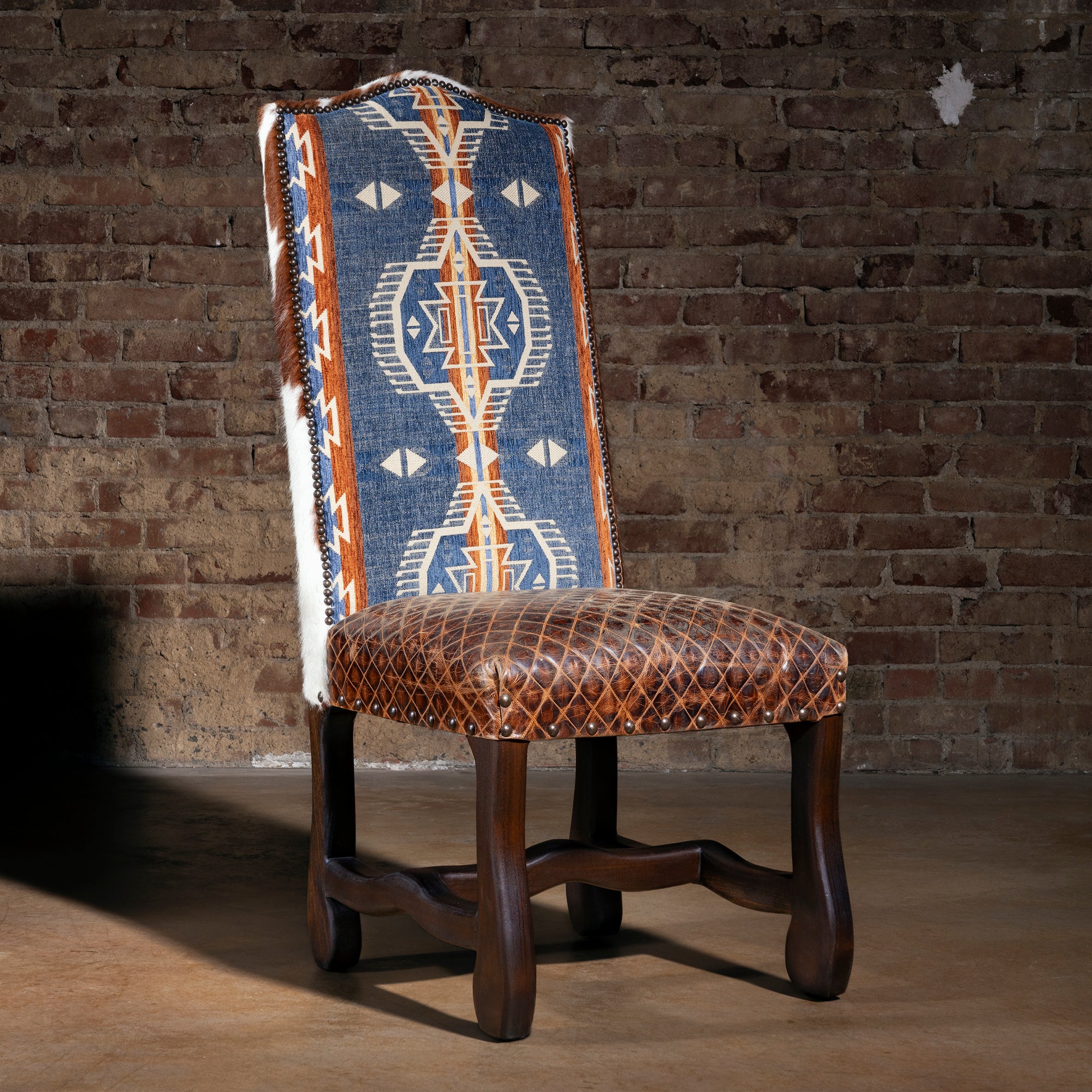 High-back Western dining chair with blue Southwestern woven fabric, quilted leather seat, nailhead trim, and dark wood legs in luxury ranch style