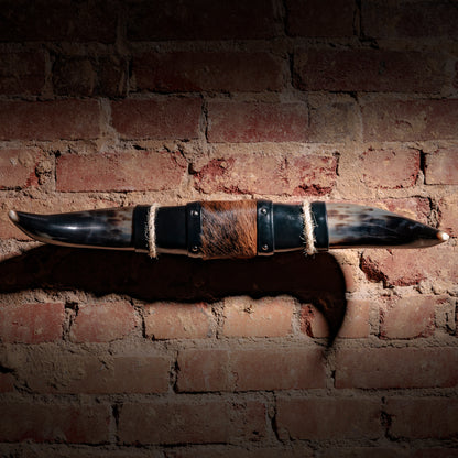 Mounted longhorn horn decor with cowhide center, black leather ends, and jute rope accents on brick wall