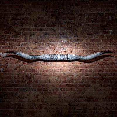 Mounted steer horns with grey spotted hide wrap and antique nailheads on brick wall
