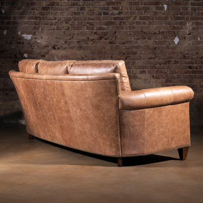 Back view of Oakley Frontier tan Western leather sofa with curved frame against brick wall