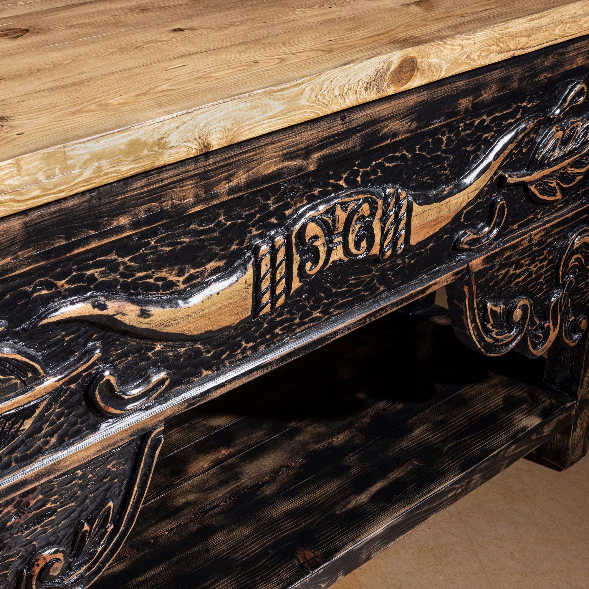 Close-up of hand-carved longhorn design and scrollwork on the apron of a reclaimed wood Western console table with rubbed dark finish.