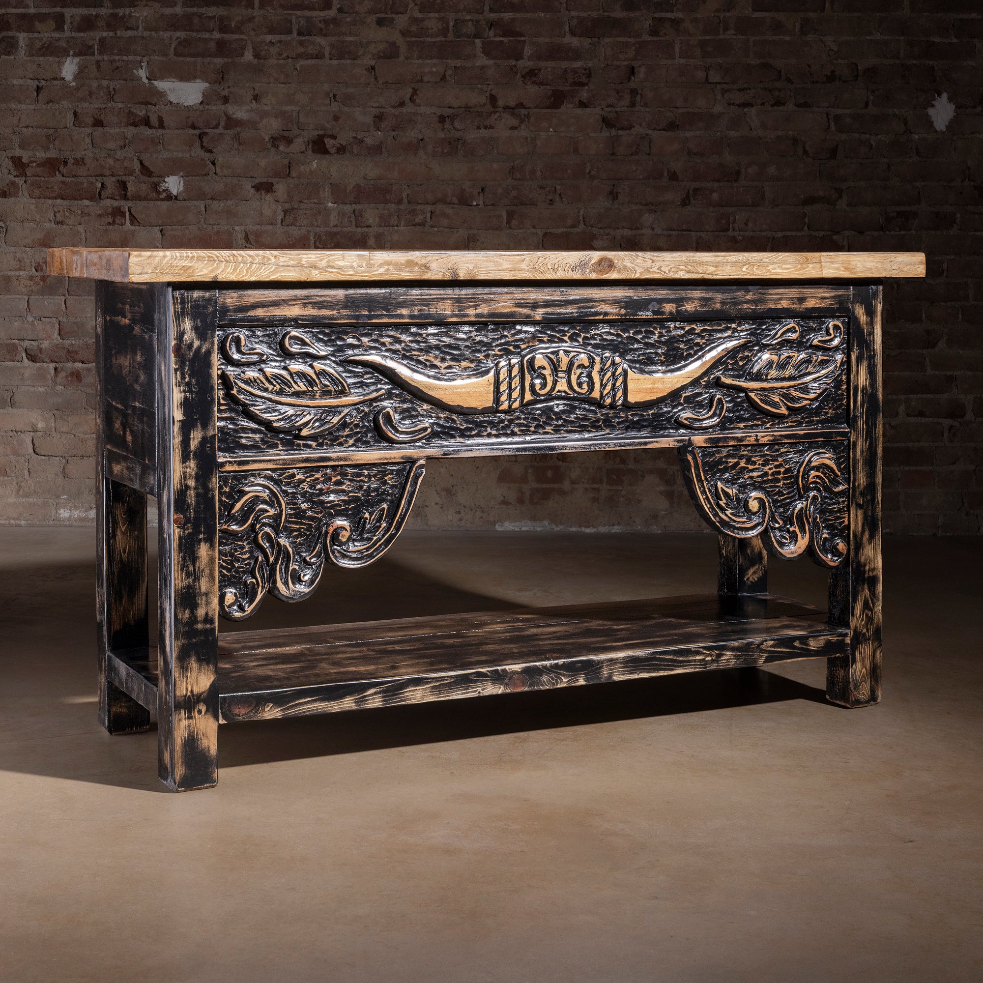 Reclaimed wood longhorn console table with hand-carved Western apron, dark rubbed finish, thick plank top, and lower storage shelf.
