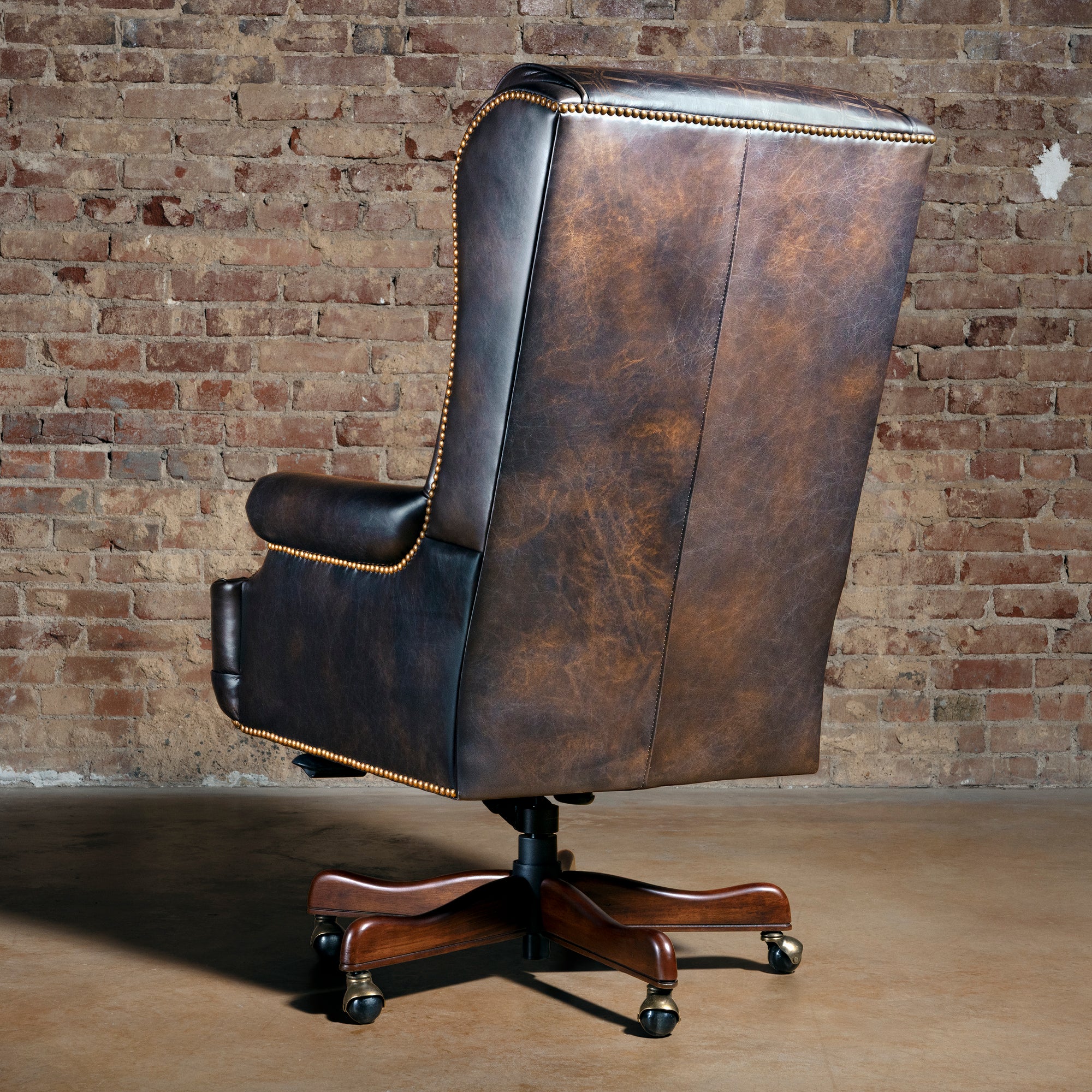 Back view of Western leather desk chair showing tall executive back, nailhead trim, and wood rolling base.