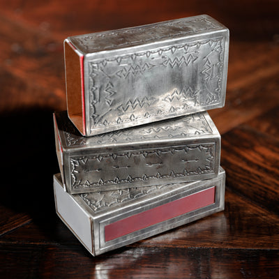Three silver matchbox holders stacked on rustic wood surface