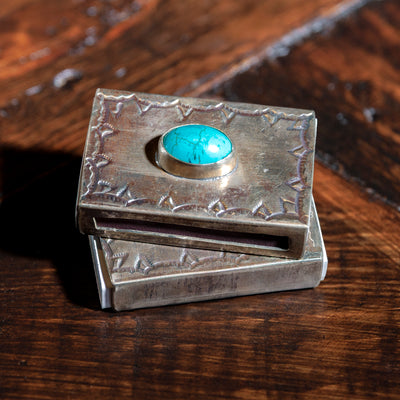 Two silver matchbox holders by J. Alexander stacked on a wooden surface
