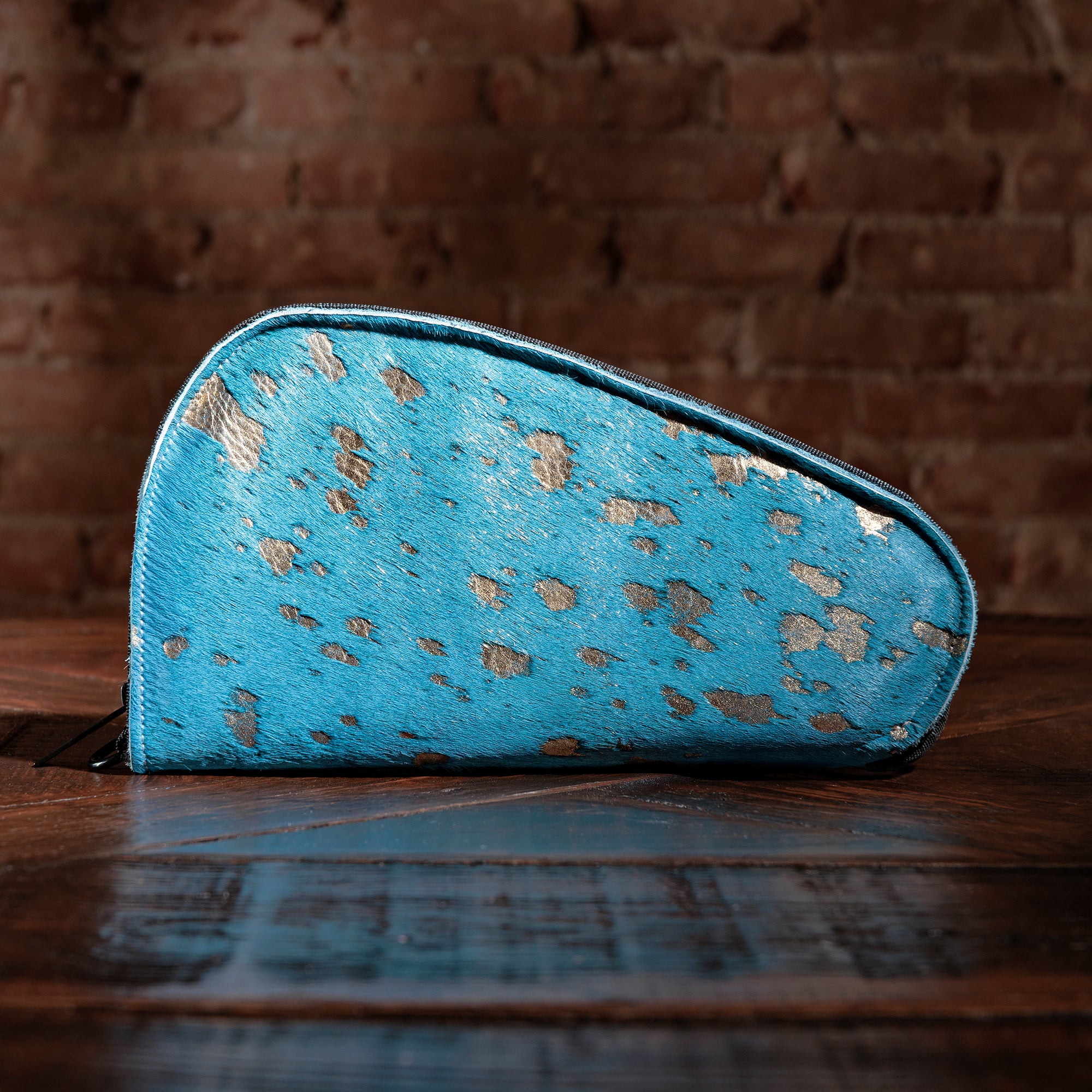 Turquoise hair-on-hide gun case with gold metallic flecks on rustic wood table