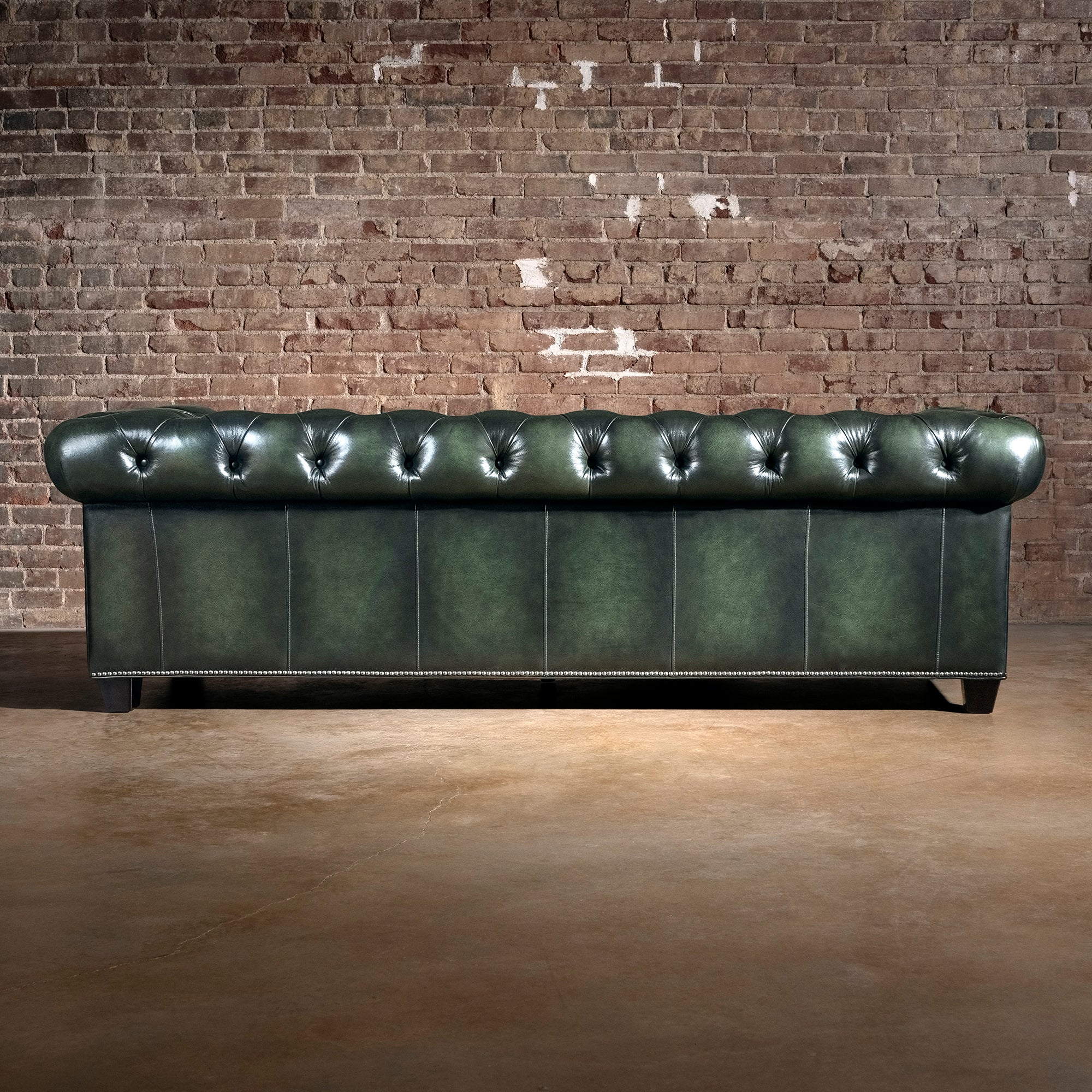 Verde Sovereign western sofa rear view with deep green leather panels, tufted back rail, nailhead trim, and dark wood feet
