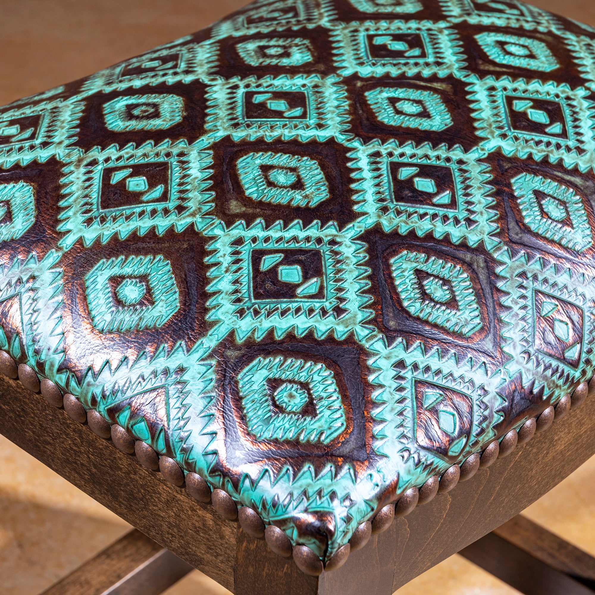 Verdigris Saddle Stool closeup of turquoise tooled leather, raised Western pattern, and bronze nailhead trim