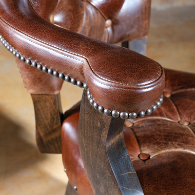 Close-up of the arm detail on a Western bar stool featuring rich brown leather and nailhead trim