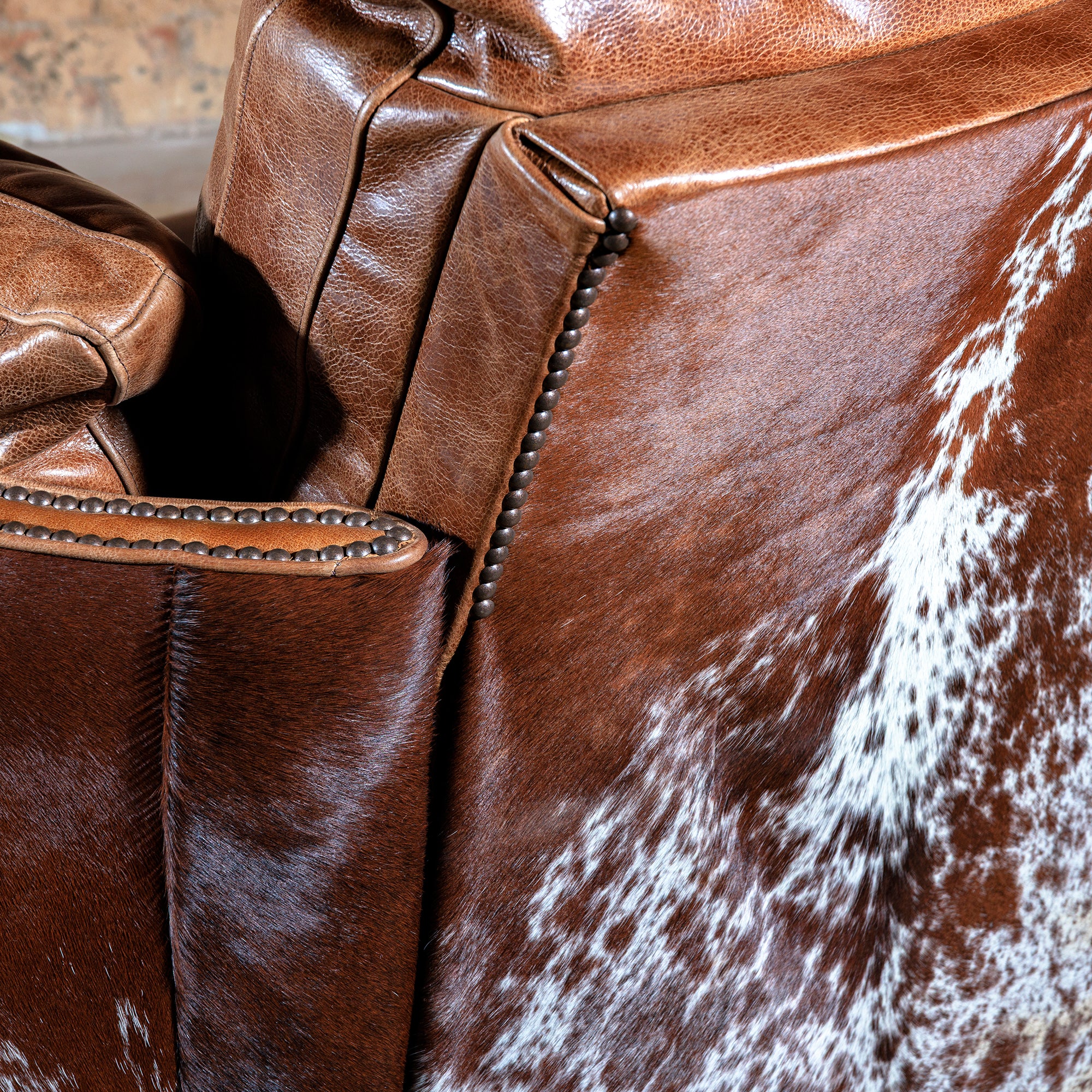 Close-up of rustic nailhead trim, brindle cowhide, and premium leather on handcrafted Western recliner