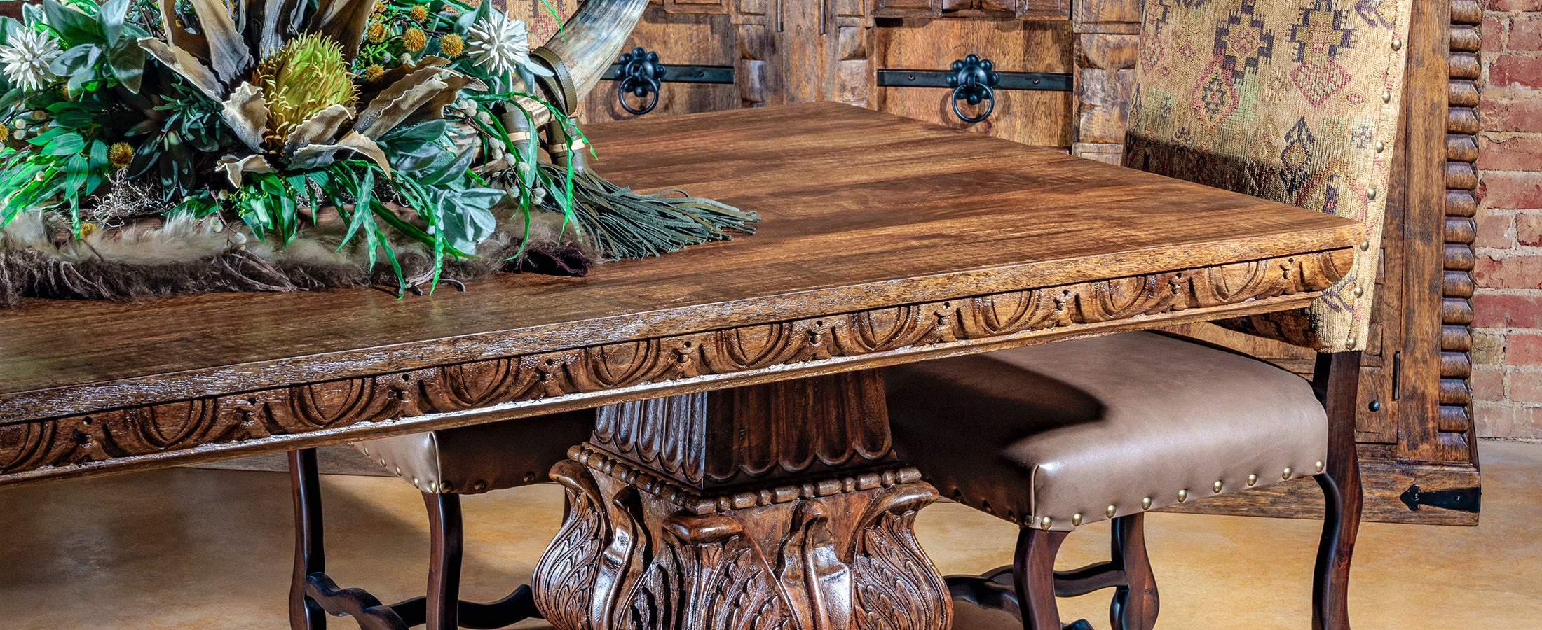Western wooden dining table with intricate carvings and a chair in a rustic setting.