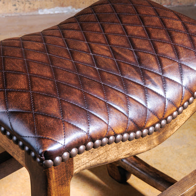 Close-up of brown quilted leather seat with diamond stitching and nailhead trim.