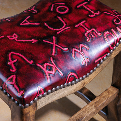 Close-up of red leather seat with embossed cattle brand designs and nailhead trim.