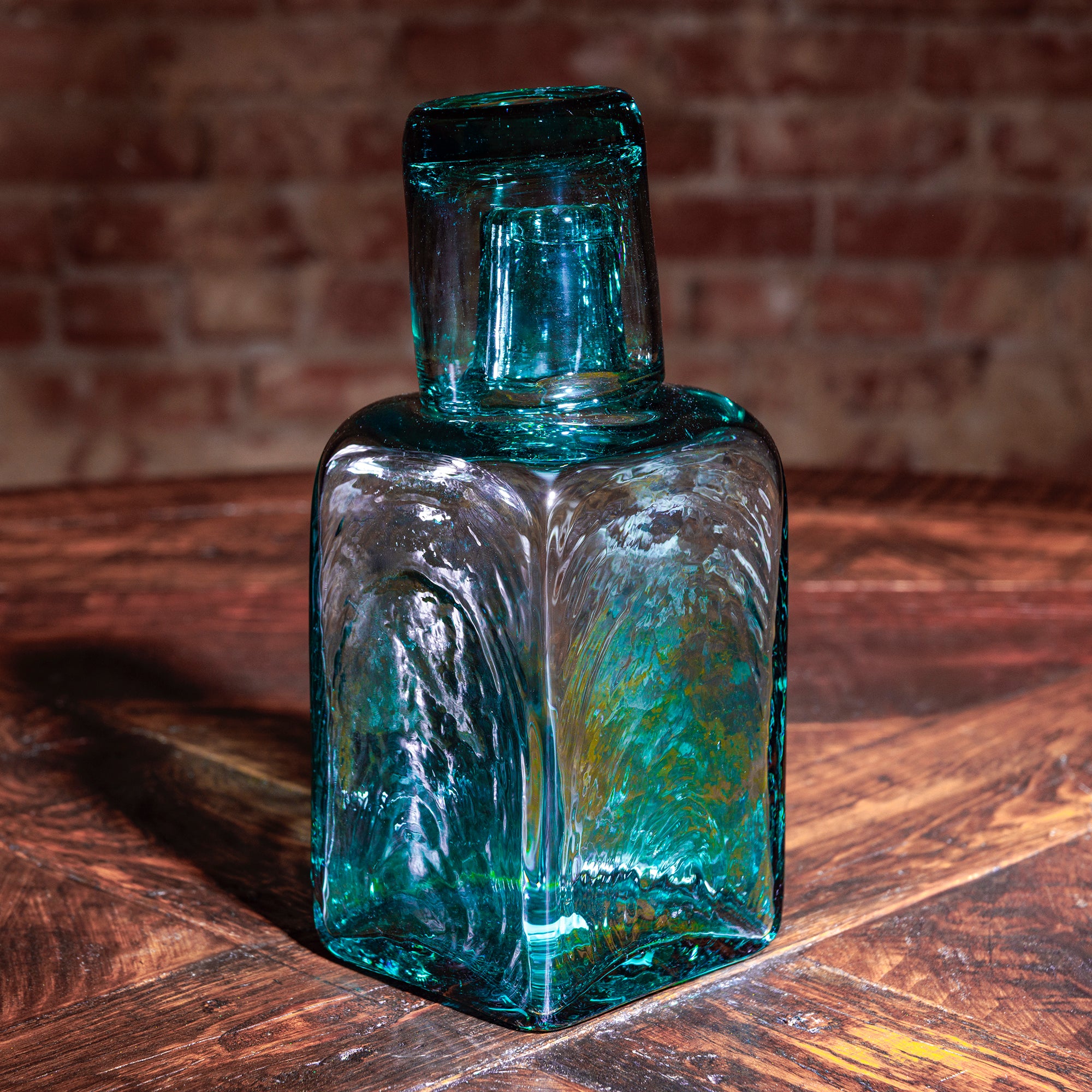 Teal handblown whiskey decanter and shot glass set on rustic wood table